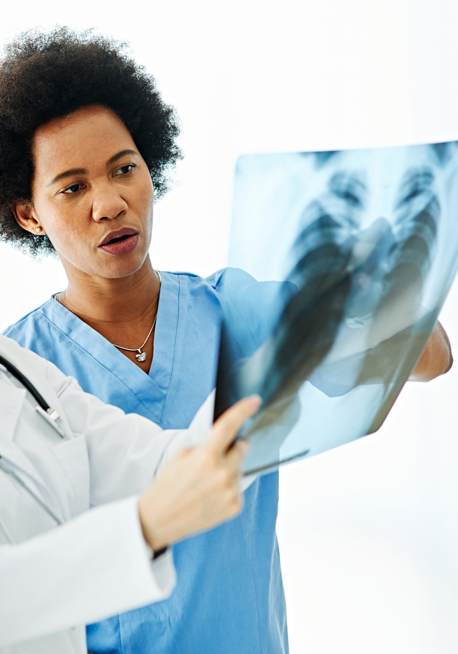 An x-ray technician in blue scrubs is holding up an e-ray to examine the image and bones.