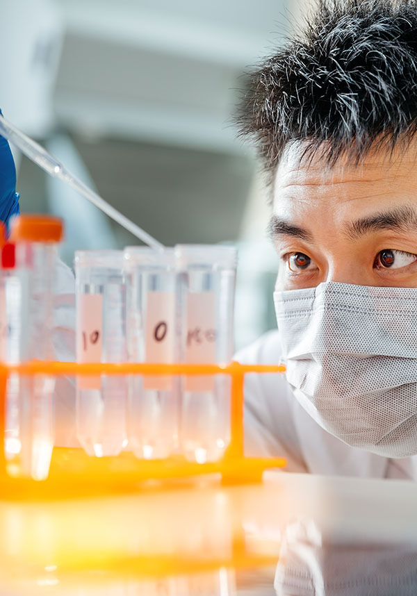 A provider in a mask, running an experiment with various compounds in test tubes.